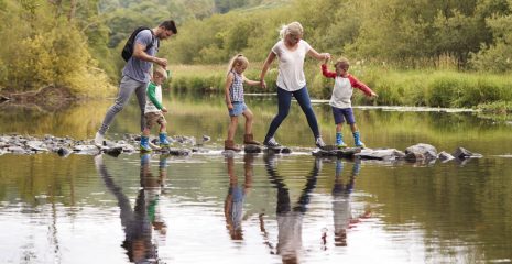 Family Crossing River Whilst Hiking In UK Lake District