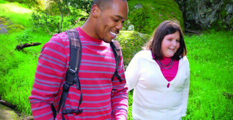 A man and a visually impaired woman walking together outdoors smiling