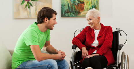 A young man sits with a mature lady in a motorised wheelchair have a discussion